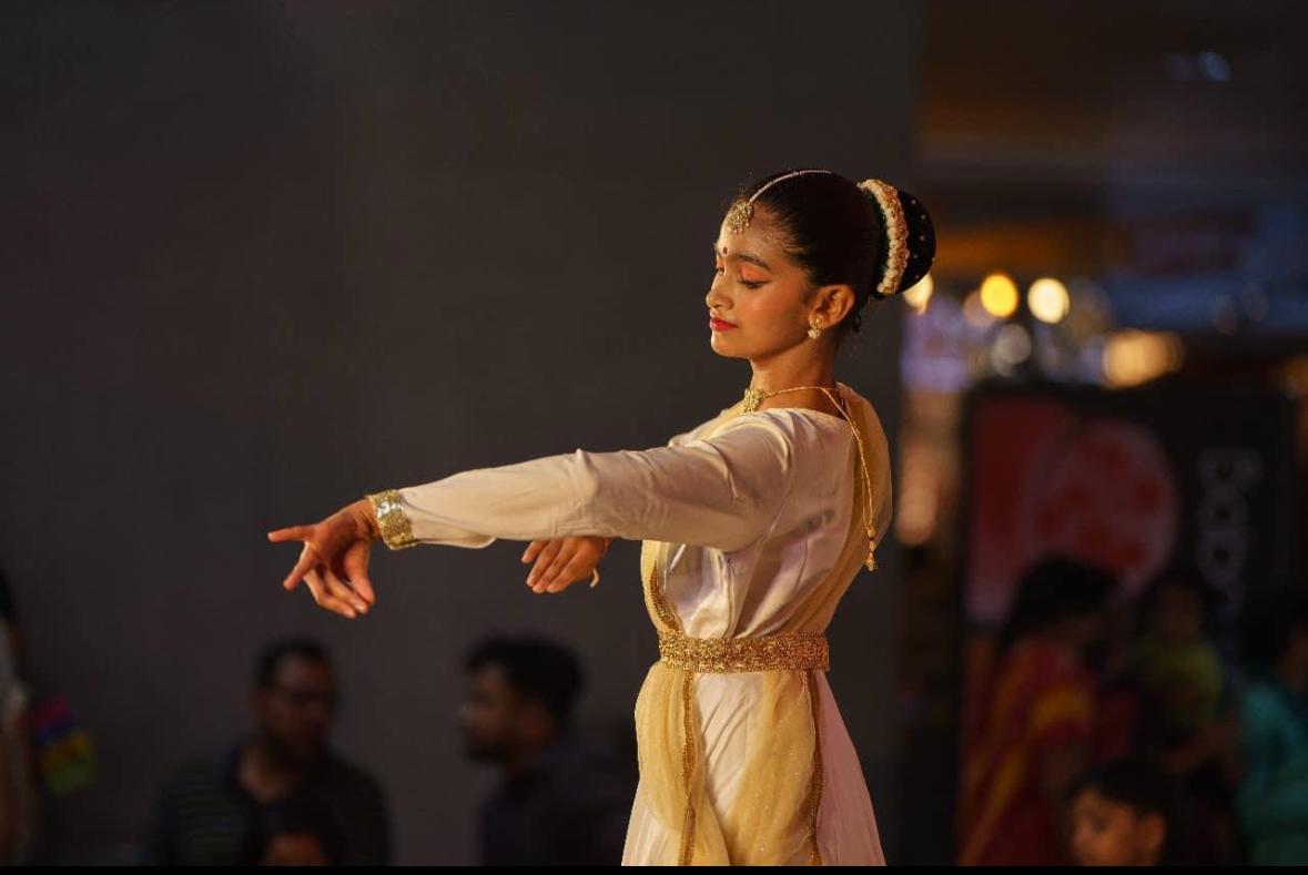 Freya performing Kathak in white and gold costume, eyes closed, arm extended